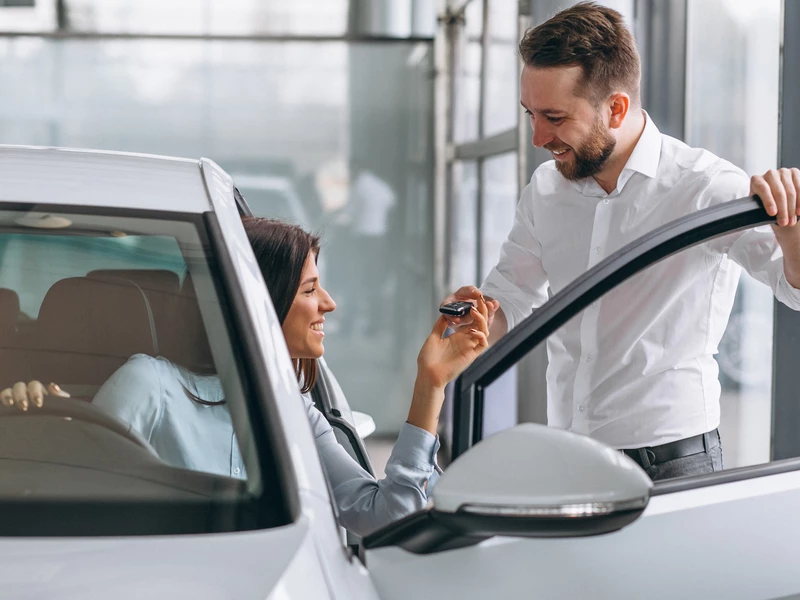 Девушка сидит в новом автомобиле мужчина подает ей ключи