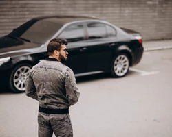 мужчина в куртке стоит возле черной машины