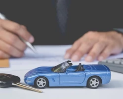 Голубой автомобиль и ключ лежит на столе, мужчина подписывает документы