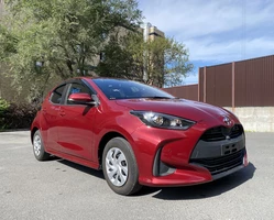 Красный тайота ярис на фоне дерева и здания, ясная погода