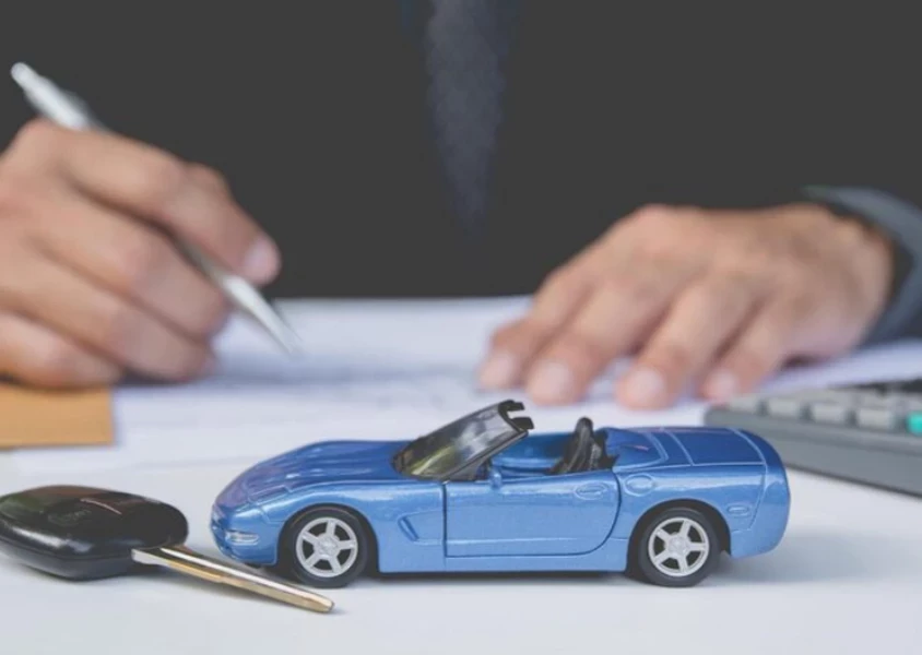 Голубой автомобиль и ключ лежит на столе, мужчина подписывает документы