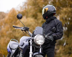 мотоциклист в черном стоит на фоне осеннего леса