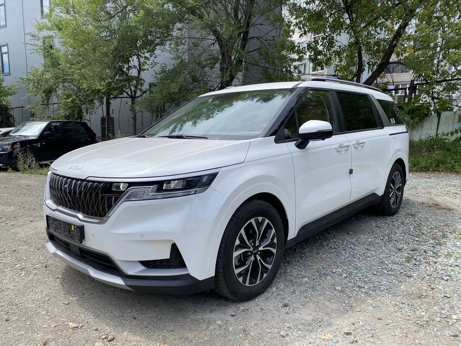 киа карнивал 4 белого цвета на фоне деревьев