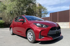 Красный тайота ярис на фоне дерева и здания, ясная погода