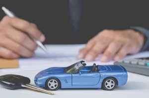 Голубой автомобиль и ключ лежит на столе, мужчина подписывает документы