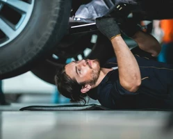 Автомеханник мужчина с бородой лежит под автомобилем и чинит ходовую часть автомобиля