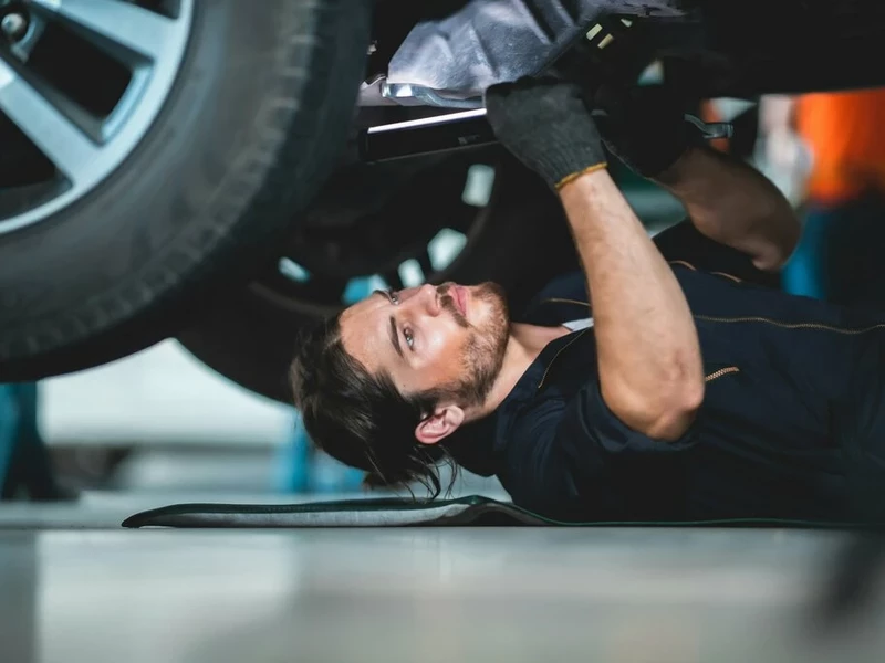 Автомеханник мужчина с бородой лежит под автомобилем и чинит ходовую часть автомобиля