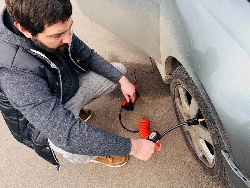 мужчина качает колесо компрессором в осенней куртке