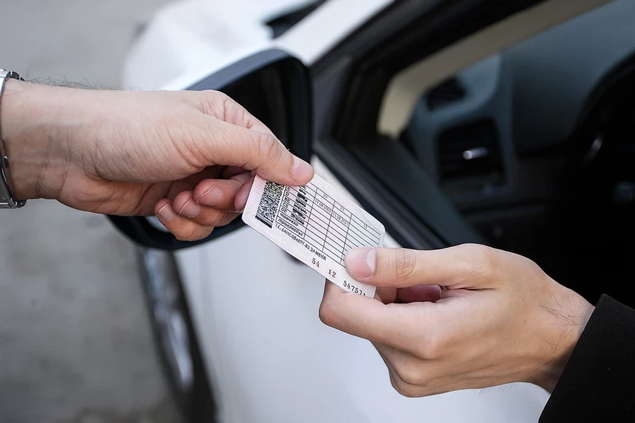 мужская рука передает водительские права водителю на фоне белой машины