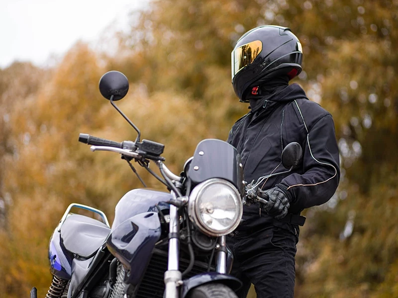 мотоциклист в черном стоит на фоне осеннего леса