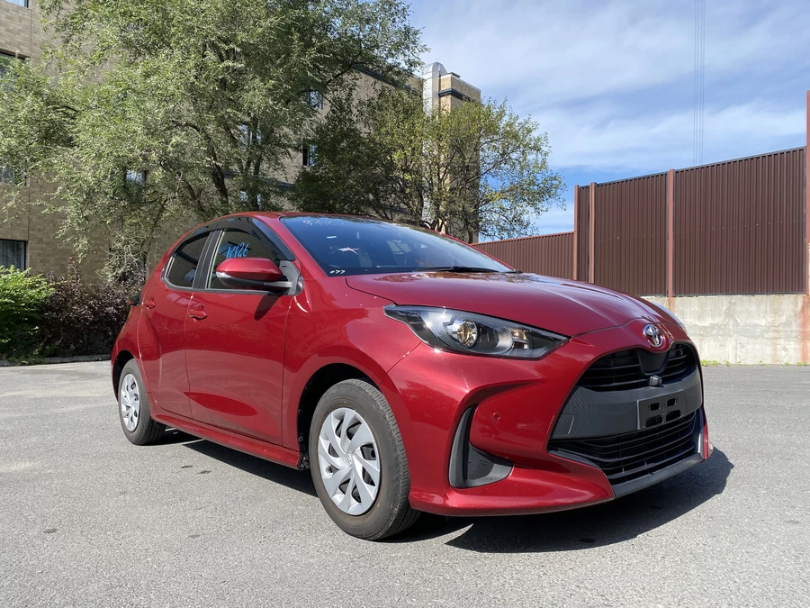 Красный тайота ярис на фоне дерева и здания, ясная погода