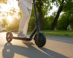 молодой парень едет на чёрном электросамокете в парке