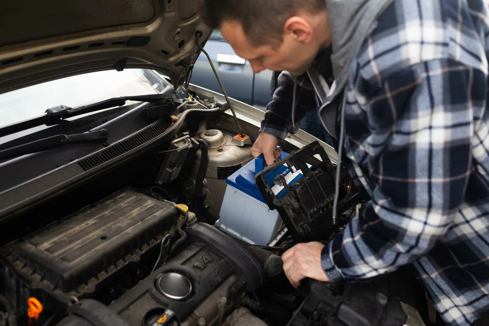 Мужчина в клетчатой рубашке меняет аккумулятор