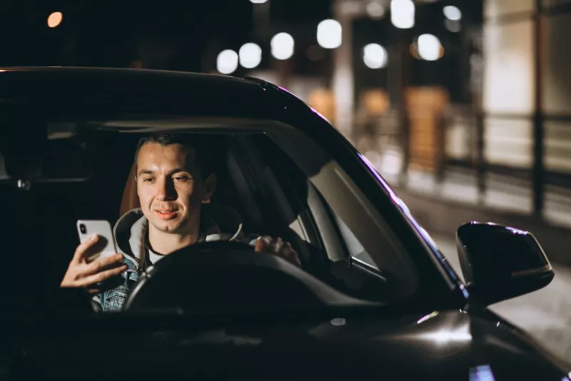 мужчина ночью смотрит в автомобиле в телефон