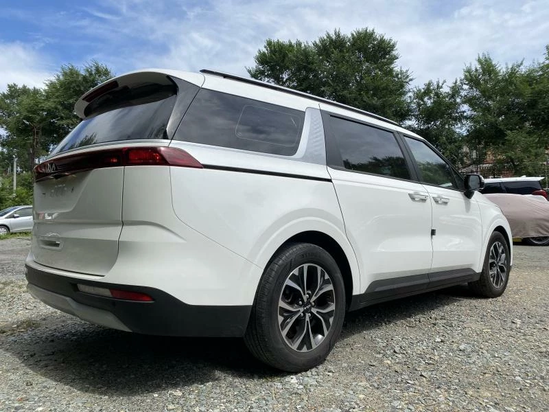 Kia Carnival четвертое поколение в белом цвете на фоне деревьев