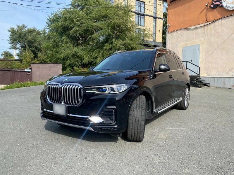 BMW X7 2019 вид сбоку на фоне дерева и здания