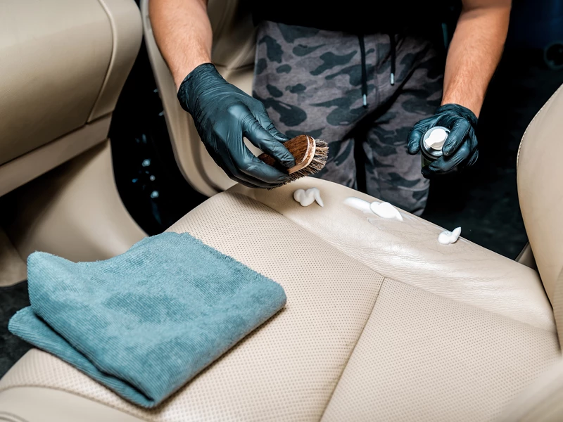 кожаный салон бежевого цвета чистит человек с щеткой