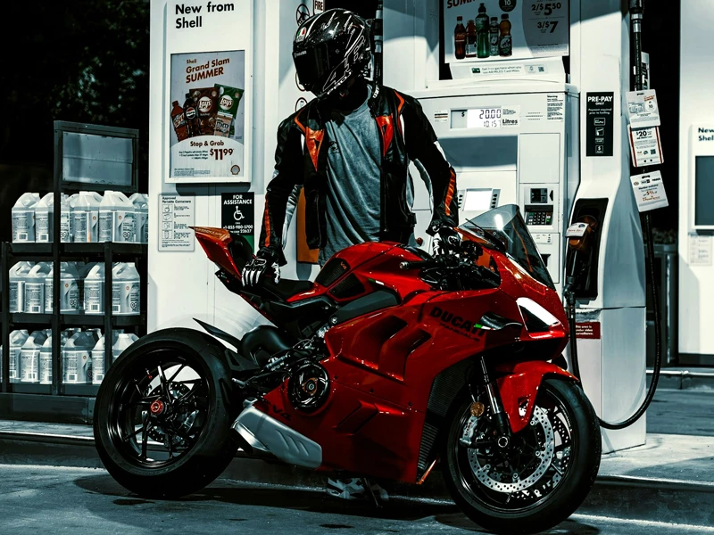 мотоциклист в черном шлеме заправляет красный мотоцикл на белой заправке